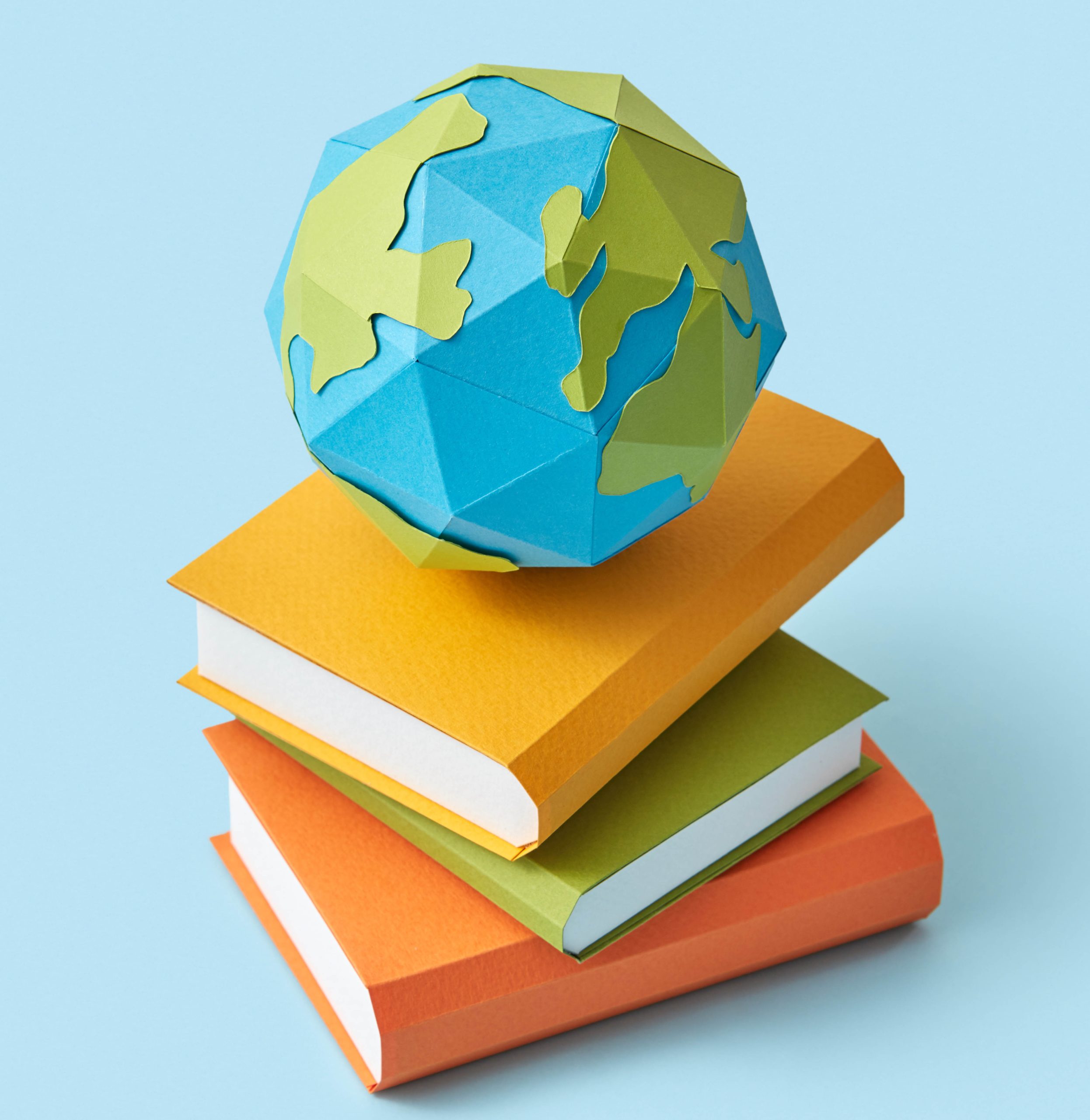 Handcraft from colored paper a stack of books with globe on the top on a pastel blue background with soft shadows, copy space. Back to school education concept.